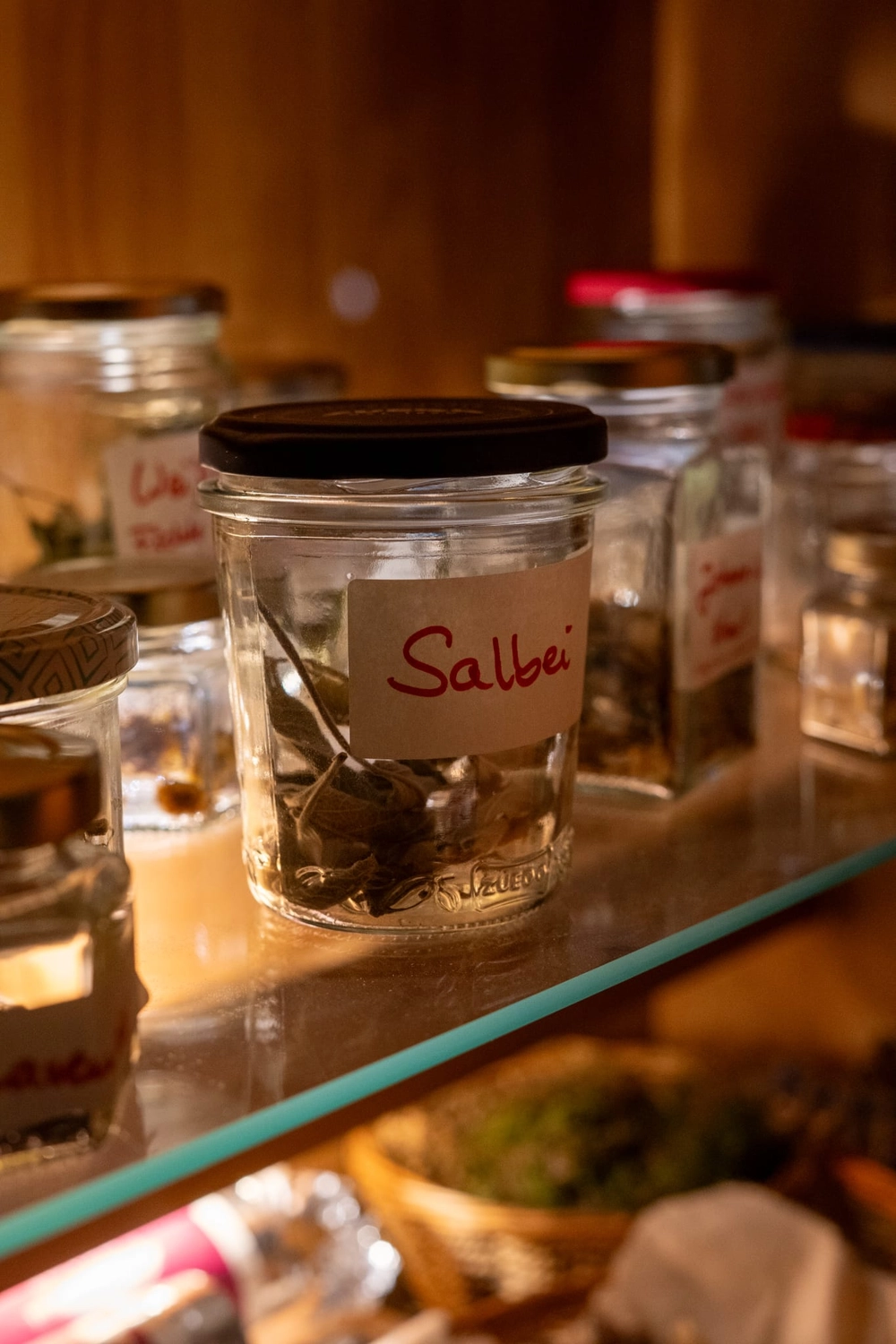 Energie Stüberl - Marianne Roßmadl - Energetische Heilarbeit und Massage - Glasgefäß mit der Aufschrift „Salbei“ mit getrockneten Kräutern auf einem Küchenregal, im Hintergrund weitere Gläser