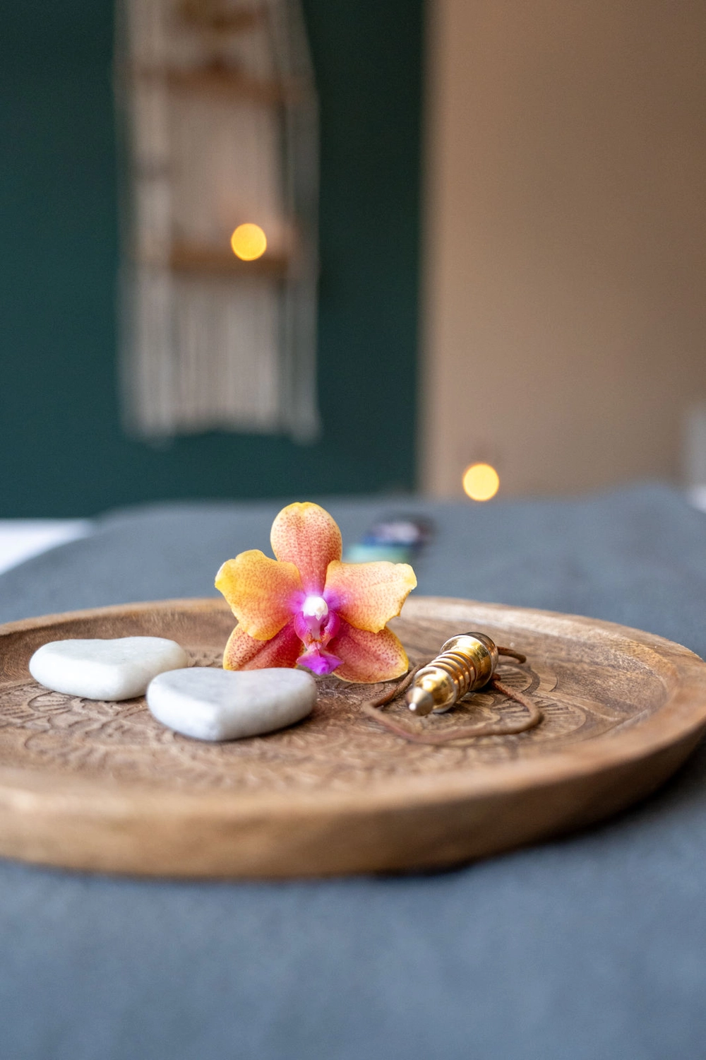 Energie Stüberl - Marianne Roßmadl - Energetische Heilarbeit und Massage - Holztablett mit zwei weißen herzförmigen Steinen, einer orangefarbenen Orchideenblüte und einem Messingpendel auf blaugrauer Oberfläche