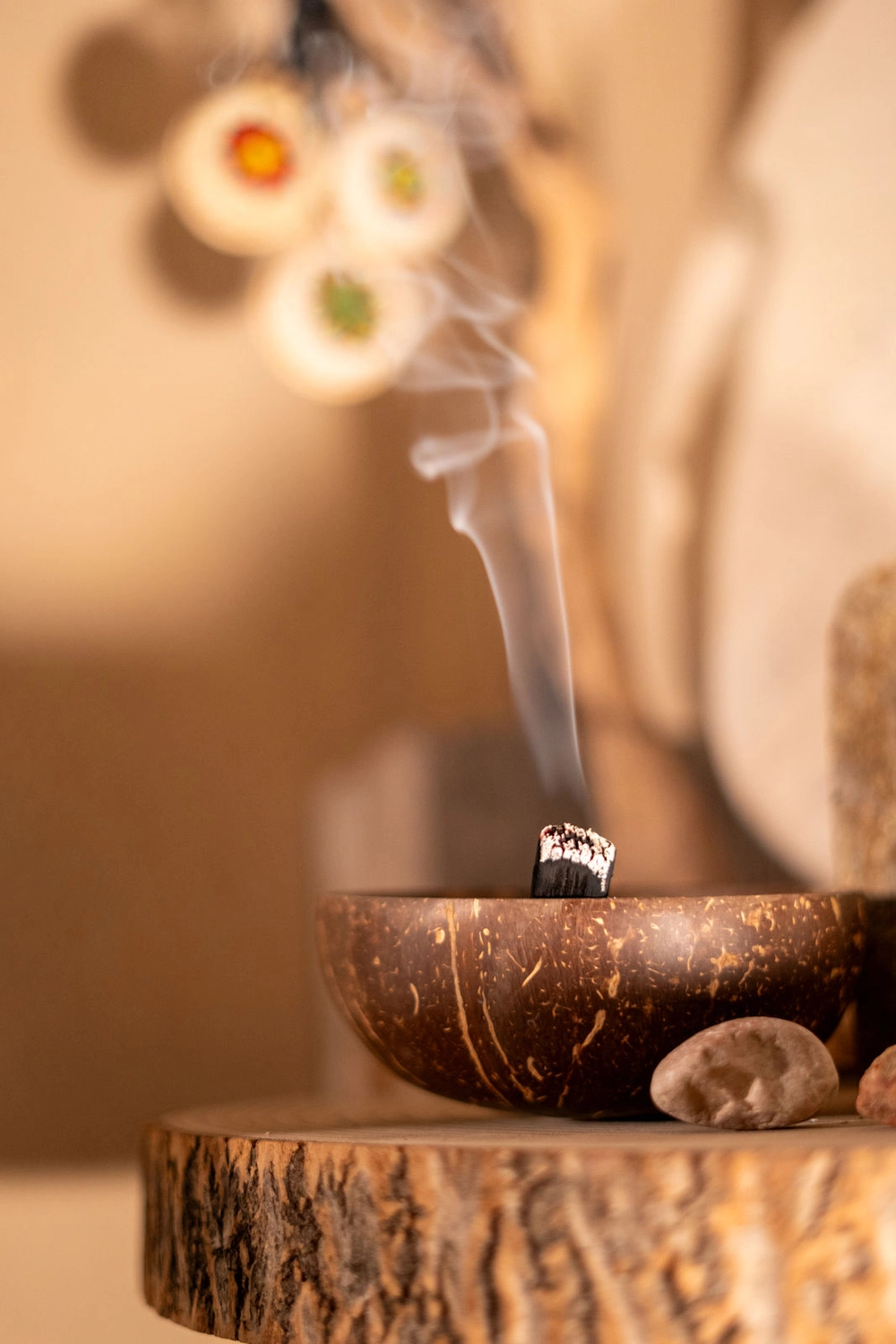 Energie Stüberl - Marianne Roßmadl - Energetische Heilarbeit und Massage - Räucherstäbchen, das Rauch ausstößt, in einer rustikalen Schale auf einer Holzoberfläche platziert, daneben glatte Steine