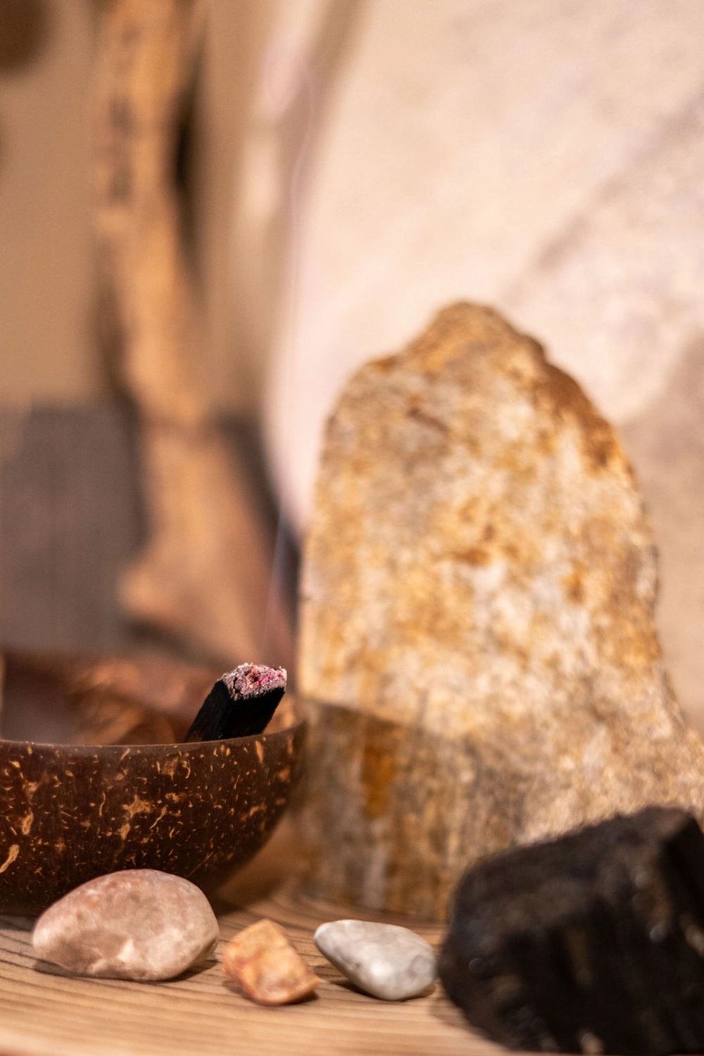 Energie Stüberl - Marianne Roßmadl - Energetische Heilarbeit und Massage - Brennender Palo-Santo-Stick, der Rauch ausstößt, in einer Holzschale mit Steinen und rustikalem Hintergrund