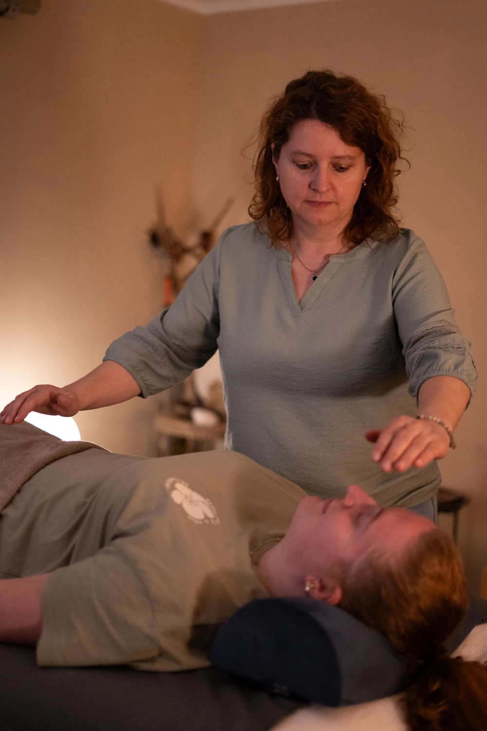 Energie Stüberl - Marianne Roßmadl - Energetische Heilarbeit und Massage - Eine Frau führt Reiki-Heilungen durch und schwebt mit den Händen über einer liegenden Person mit geschlossenen Augen