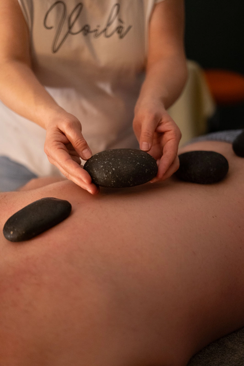 Energie Stüberl - Marianne Roßmadl - Energetische Heilarbeit und Massage - Person legt während einer Hot-Stone-Massagetherapie glatte schwarze heiße Steine ​​auf einen nackten Rücken