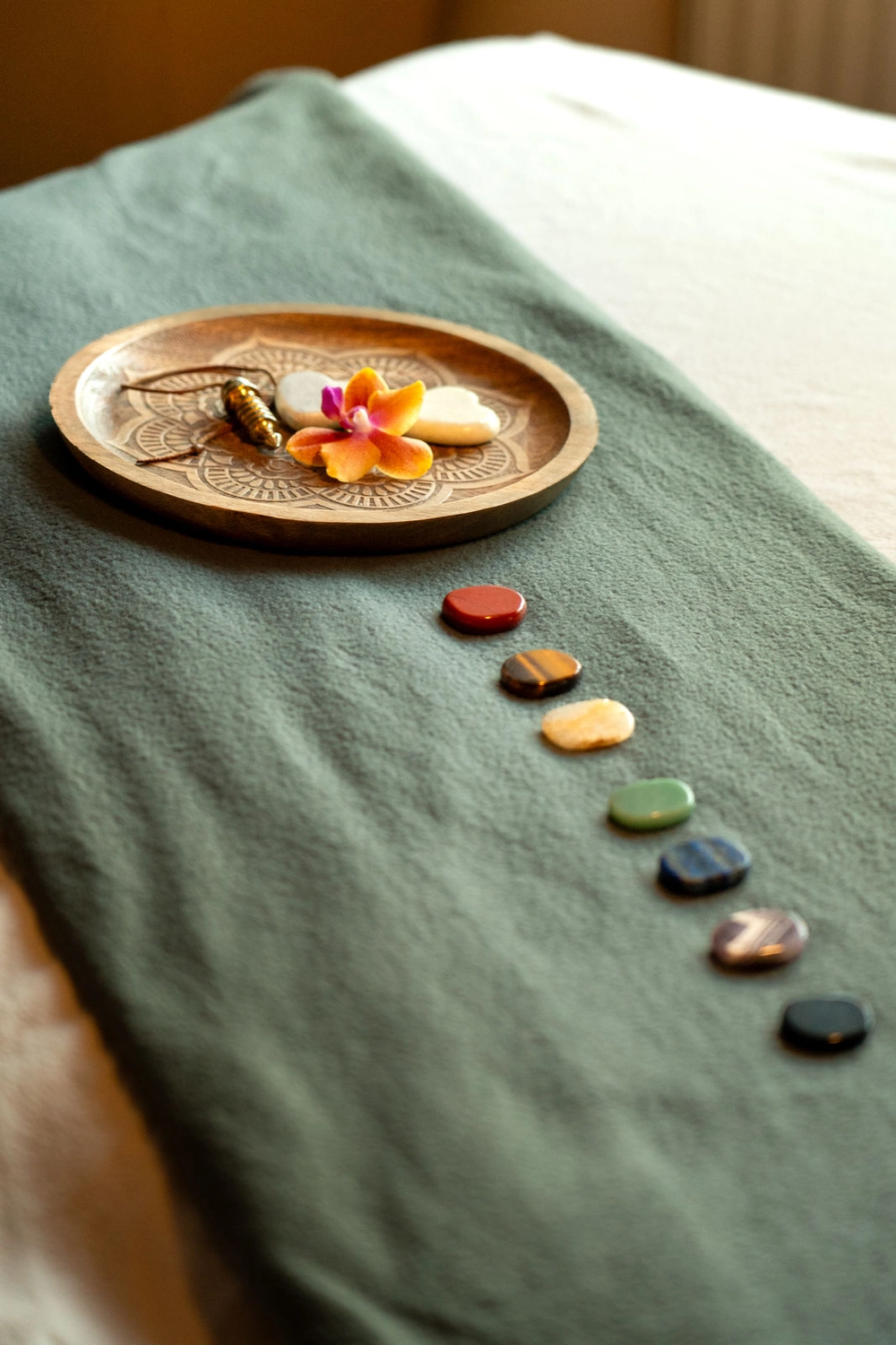 Energie Stüberl – Marianne Roßmadl – Energetische Heilarbeit und Massage – Eine Reihe bunter, polierter Steine ​​auf einem grünen Tuch, darauf ein Holztablett mit herzförmigen Steinen und einer orangefarbenen Orchideenblüte